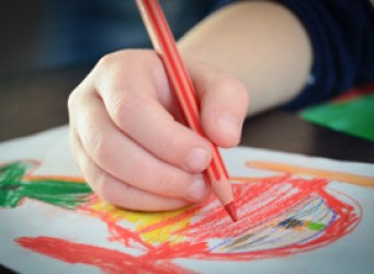 Imagen de la mano de un niño/a dibujando con lápices de colores