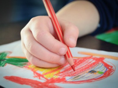 Imagen de la mano de un niño/a dibujando con lápices de colores