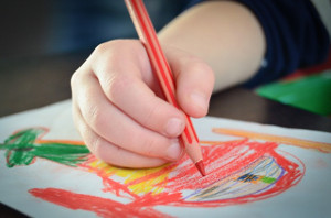 Imagen de la mano de un niño/a dibujando con lápices de colores